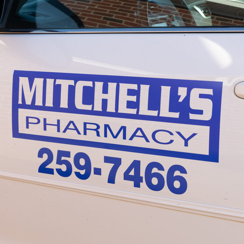 The Mitchell's Pharmacy logo and phone number on the door of a Mitchell's Pharmacy delivery vehicle